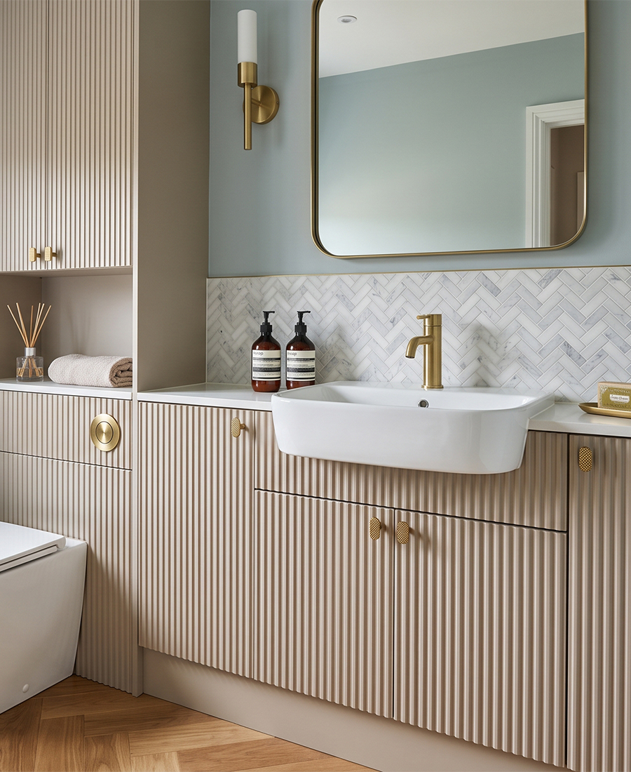 Brockenhurst cashmere fluted bathroom vanity and matching cabinets with brass handles, a white basin and a brass-framed mirror